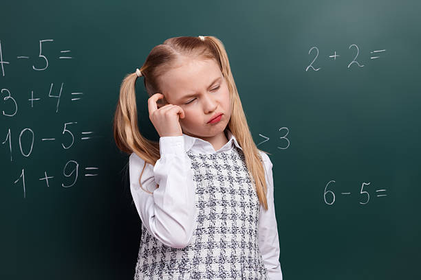 istock Thoughtful young girl in school uniform solving math equations on green chalkboard, representing education and childhood learning 2220681652