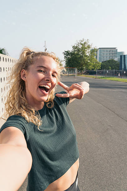 Young woman with blonde curly hair taking a selfie while making peace sign gesture in a park in barcelona