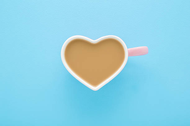 White heart shape cup of fresh coffee with milk on light blue table background. Pastel color. Closeup. Top down view.