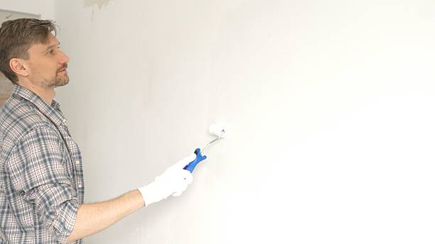 istock Man professional painter wearing checkered shirt, is rolling white paint on apartment wall, transforming interior space with steady strokes during comprehensive home renovation 2220686822