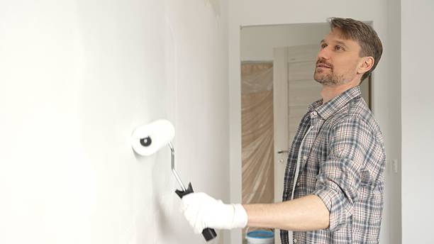 istock Middle aged man wearing checkered shirt, is rolling white paint on apartment wall with paint roller, transforming interior space with steady strokes during comprehensive home renovation 2220687001