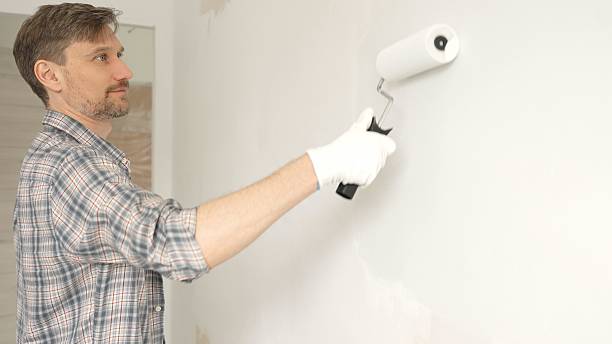 istock Man professional painter wearing checkered shirt, is rolling white paint on apartment wall with paint roller, transforming interior space with steady strokes during comprehensive home renovation 2220687183