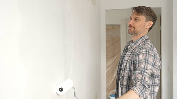 istock Middle aged man wearing checkered shirt, is rolling white paint on apartment wall with paint roller, transforming interior space with steady strokes during comprehensive home renovation 2220687316