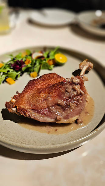 istock Enjoying crispy French classic dish — Duck Confit served with arugula, apricot, beetroot, and balsamic glaze at a bistro restaurant, nightlife vibe, black background, white table, close-up detail 2220687351