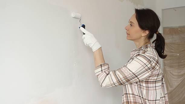 istock Painter woman wearing gloves is skillfully applying paint to a white wall with a roller in an apartment undergoing renovation, transforming the space with her creative touch 2220687464