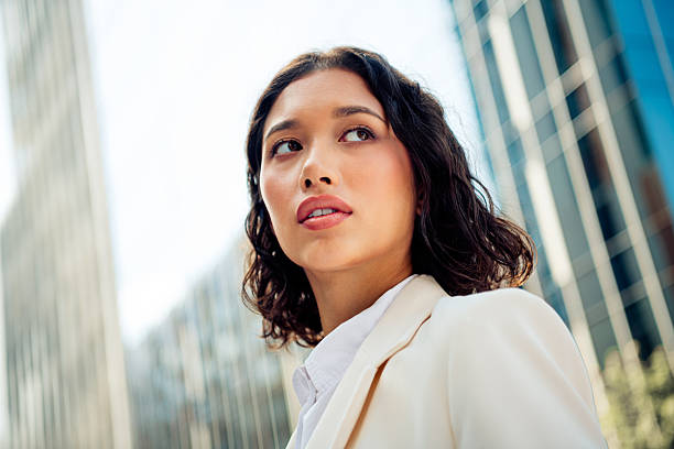 istock Professional young businesswoman looking upward in modern urban setting with sunlight and high rise buildings in summer 2220688708