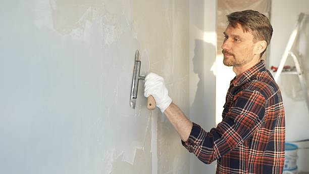 istock Male construction worker wearing protective gloves smoothing plaster onto wall surface during home renovation using professional trowel tool 2220688726