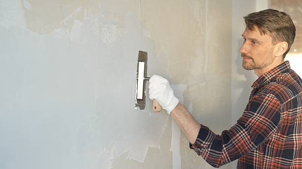 istock Male construction worker wearing protective gloves smoothing plaster onto wall surface during home renovation using professional trowel tool 2220688817