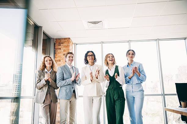 istock Professional team clapping during a meeting in a corporate office setting with large bright windows and modern interiors 2220689334