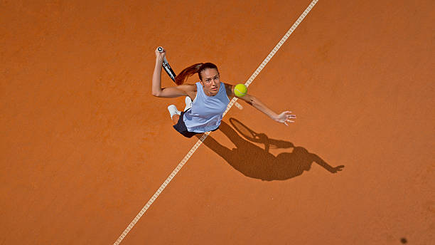 istock Athletic Female Tennis Player Serving On Clay Court Under Bright Sunlight With Dramatic Shadow 2220693048