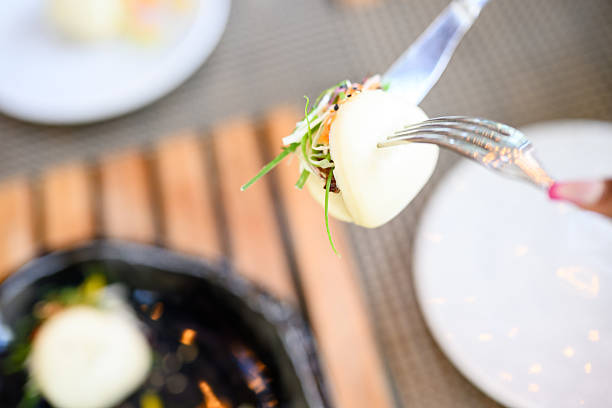 Closeup shot highlighting the detail and texture of a pork bao bun made with pulled pork, daikon slaw and an exotic bell pepper topping on a restaurant table.