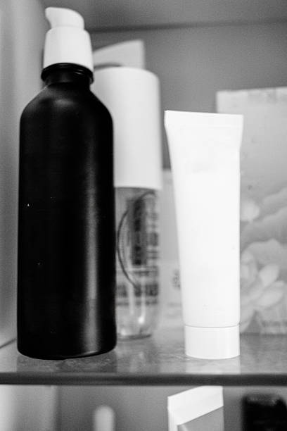 A monochrome image featuring a tall lotion bottle alongside tube-shaped cleanser products, organized on a bathroom shelf for daily hygiene.