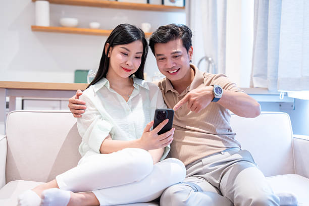 istock Couple relaxing at home browsing on mobile phone pointing at the screen enjoying their time 2220697512