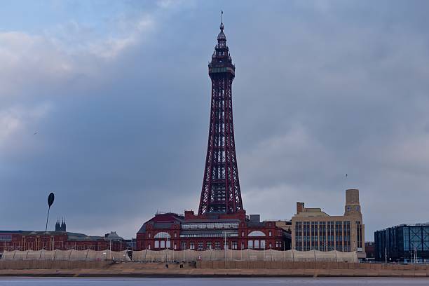 istock A tall, ornate tower stands against a cloudy sky, surrounded by lower buildings. 2220697924