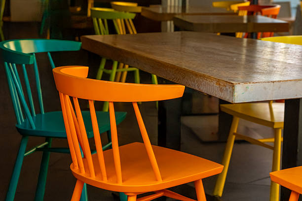 Brightly colored chairs in vibrant shades of orange, turquoise, and yellow encircle a weathered wooden table in a lively cafe, creating an inviting atmosphere for guests.