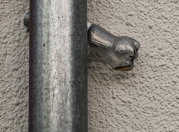 A striking glass hand ornament intertwines with a metal pipe fixed against a rough wall, blending functional elements with a whimsical touch. This fusion highlights creativity in urban environments.
