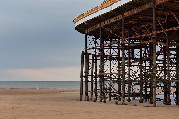 istock A pier's supports stand exposed on a sandy beach under a cloudy sky. 2220698016