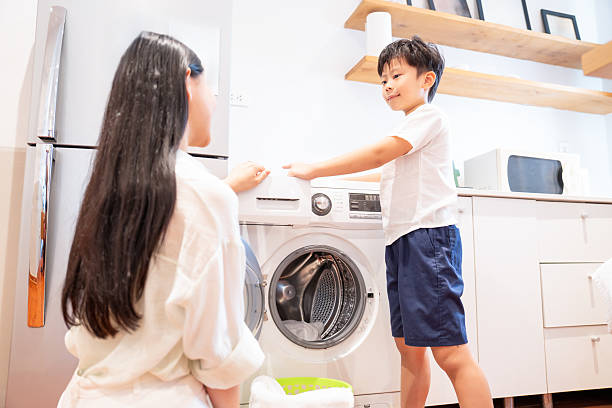 istock Mother and son using laundry machine Woman and boy preparing for laundry together at home 2220701057