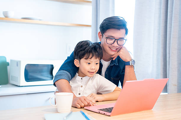 istock Father and son bonding over a laptop screen smiling at home in a light-filled kitchen space 2220702062