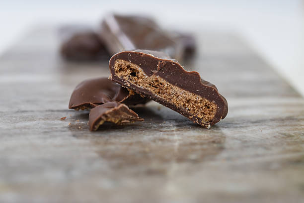 istock Chocolate Covered Biscuit Piece, broken in half to clearly show its textured, crumbly interior with hick layer of chocolate coating isolated on marble side view of sweet dessert 2220703895