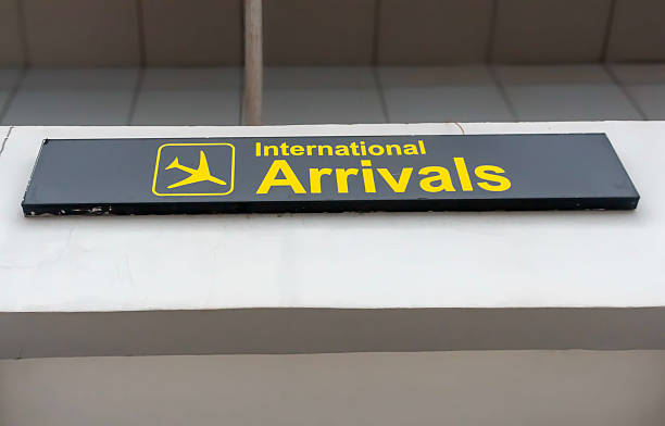 International arrivals signboard in the airport in vivid yellow letters on black backing with the sign of a descending plane in a square box