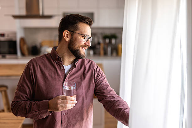 istock A bearded man wearing glasses drinks water from a glass in a modern kitchen. He enjoys a refreshing moment, focusing on hydration, wellness, and a healthy lifestyle in a bright, cozy home environment. 2220704737