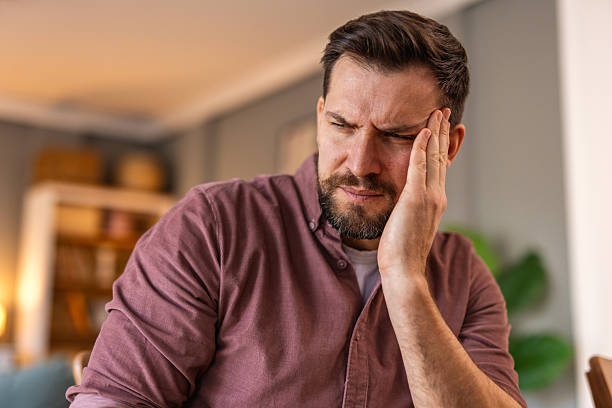 istock Closeup of man suffering from headache at home, touching his temples, copy space, blurred background. Migraine, headache, stress, tension problem, hangover concept 2220704761