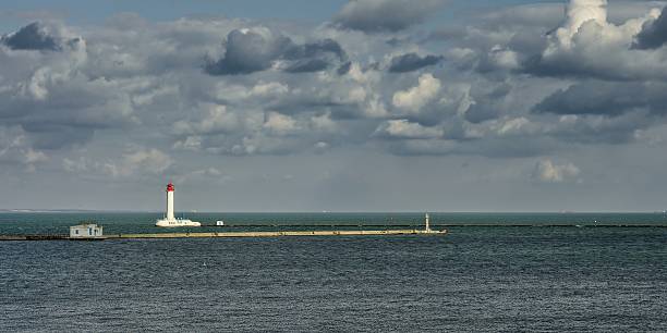 istock A striking coastal scene with a lighthouse guiding ships through calm waters under a cloudy sky. 2220707408