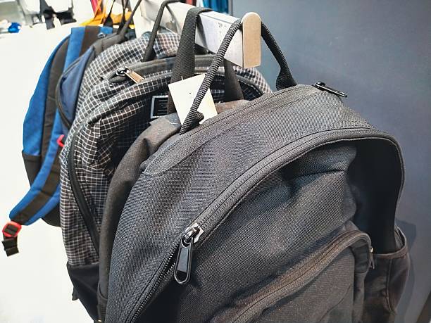 A collection of backpacks hang on a rack, showcasing various designs and colors, ready for purchase in a retail setting.
