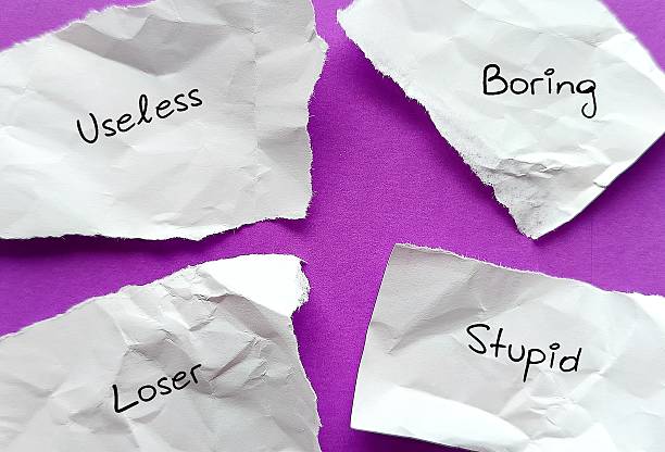 Torn crumples paper pieces with text label - loser stupid useless boring - Low self-esteem person tended to use negative labels to describe themselves - self-sabotage by believing unfair negative labels