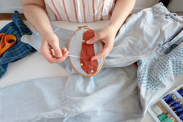 A senior woman of 60 years of average age with gray hair is comfortably dressed on the couch at home doing her favorite hobby which is making clothes on her machine