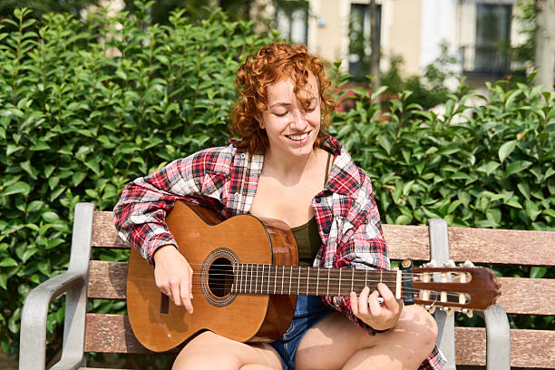 istock Young redhead woman playing acoustic guitar on park bench 2220714548