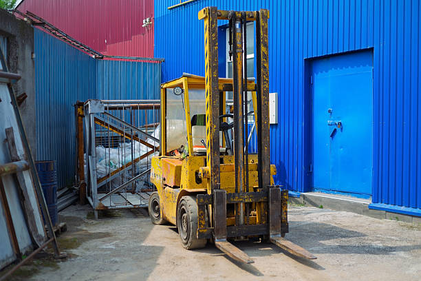 Old yellow forklift parked near a colorful warehouse building with a pile of garbage in a metal container