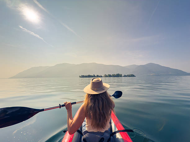 Woman paddling kayak on calm lake under clear skies. Serene outdoor adventure with scenic mountain view. Leisure activity embracing nature's beauty.