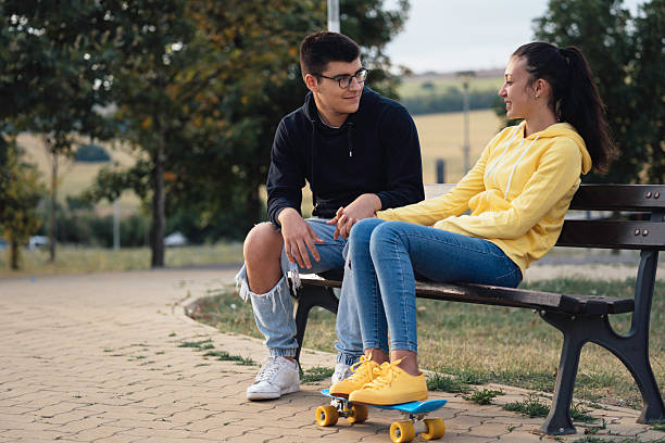 istock Young Couple Sitting on a Bench with a Skateboard 2220720553