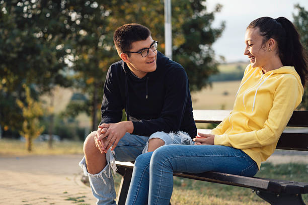 istock Young Couple Sitting on a Bench in the Park 2220720593