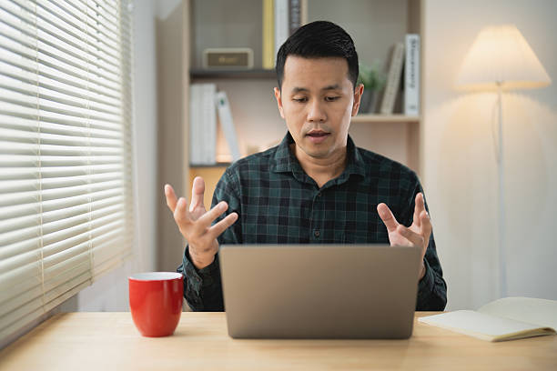 istock Young man using laptop at desk expressing emotions while communicating online in modern workspace with natural light and minimalistic decor 2220725420