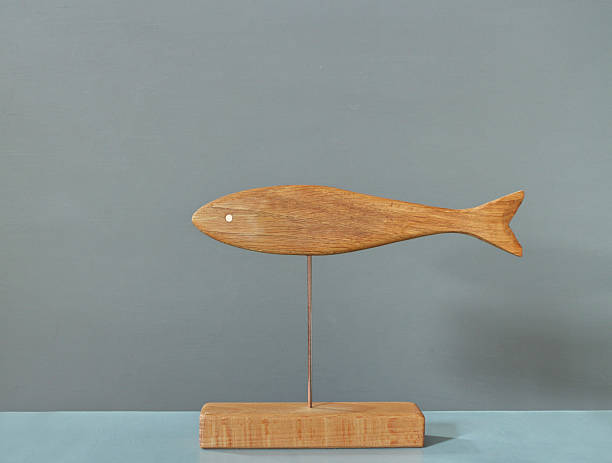 Sardine fish, wooden sculpture of a fish with a bright copper eye on a thin stand, pronounced texture of oak and beech, handmade