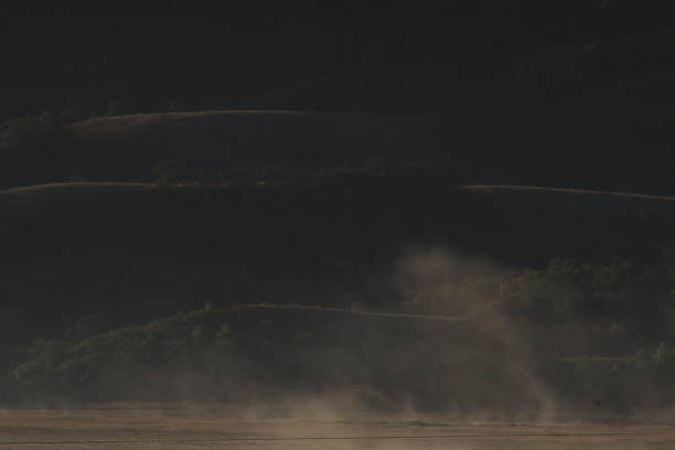The fog lifts as the sun comes up in the valley near the hay field.