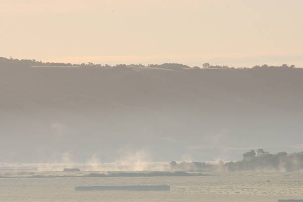 The fog lifts as the sun comes up in the valley near the hay field.