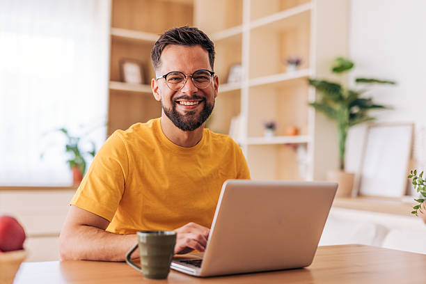 istock Young man smiling and working from home on his laptop 2220730129