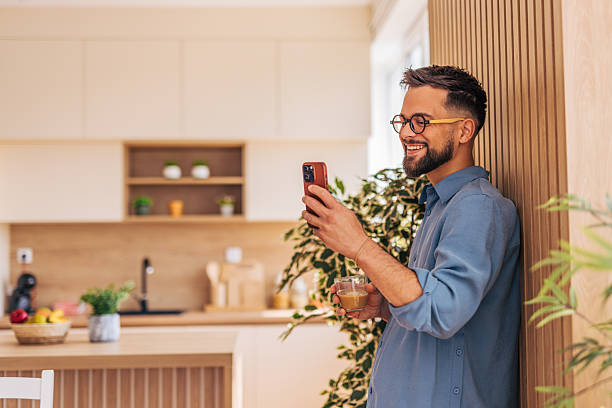 istock Young man enjoying a coffee break and browsing his smartphone in his modern kitchen 2220730522