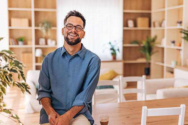 istock Young man smiling and sitting at the table in his modern apartment 2220730745
