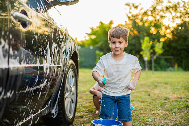 Two young brothers washing a car outdoors on a sunny day, enjoying the moment while learning valuable lessons about teamwork and responsibility through playful family activity