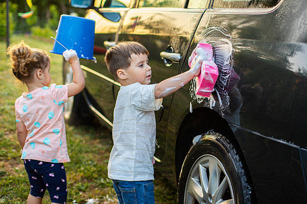 Male and female teenagers splash one another while playing in the water during a car wash fundraiser. A girl is holding a spray bottle while getting soaked by her friends.