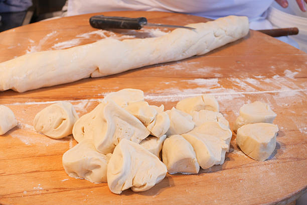 Baker shapes and cuts dough pieces on a floured wooden board.