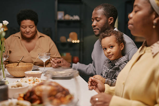istock Portrait of Black Boy on Fathers Lap Praying before Festive Dinner 2220740317