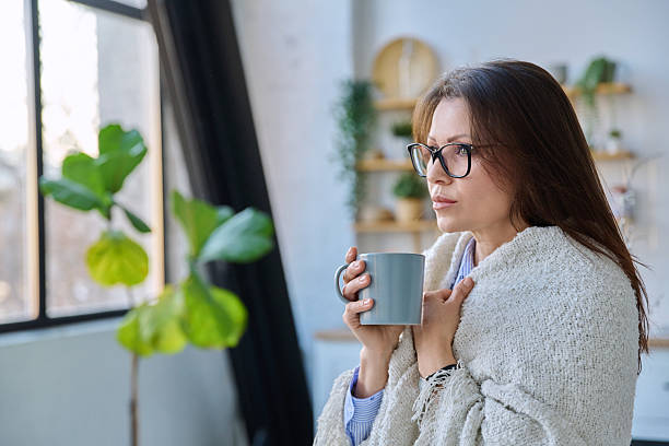 istock Relaxed middle aged woman with mug under blanket in home interior 2220742344