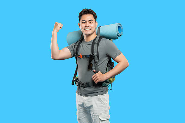 istock Enthusiastic hiker with backpack shows off arm muscles against a bright blue background 2220743134