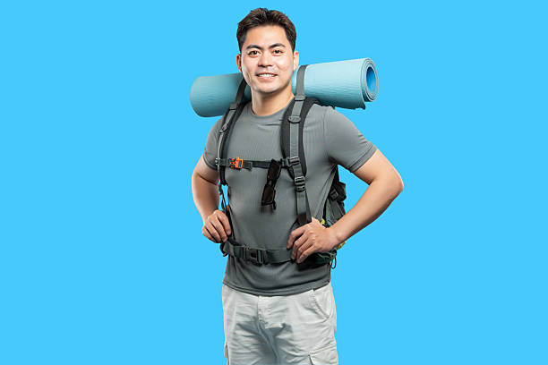 istock Smiling Asian hiker with backpack and sleeping mat poses against a vibrant blue background 2220743197
